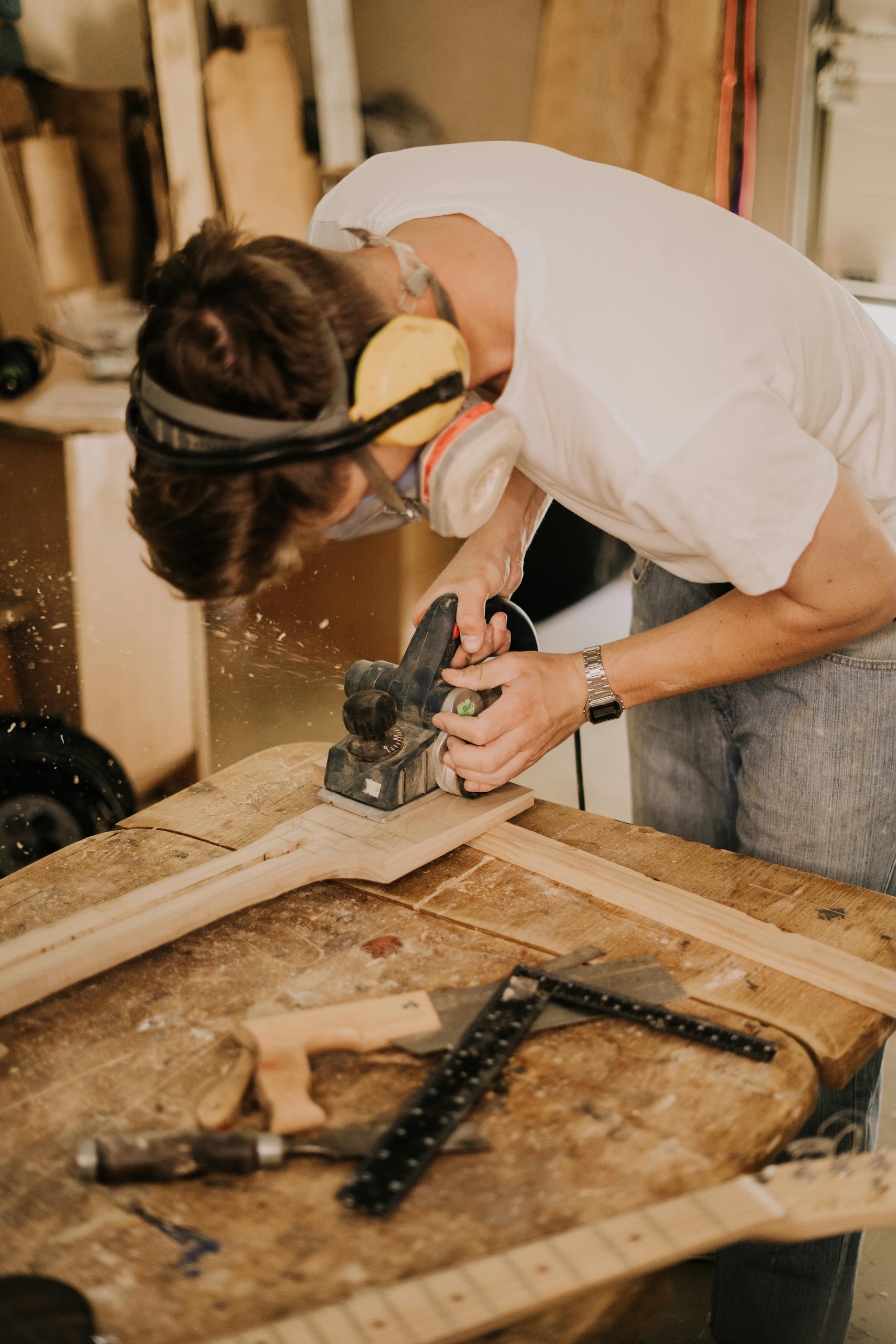 Artisan avec un masque en train de poncer une pièce de bois dans son atelier.