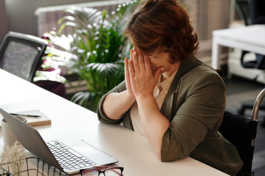 Femme devant un ordinateur portable se tenant le visage entre les mains.