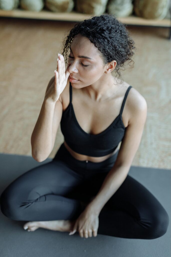 Femme assise sur un tapis pratiquant un exercice de respiration pour la gestion du stress.