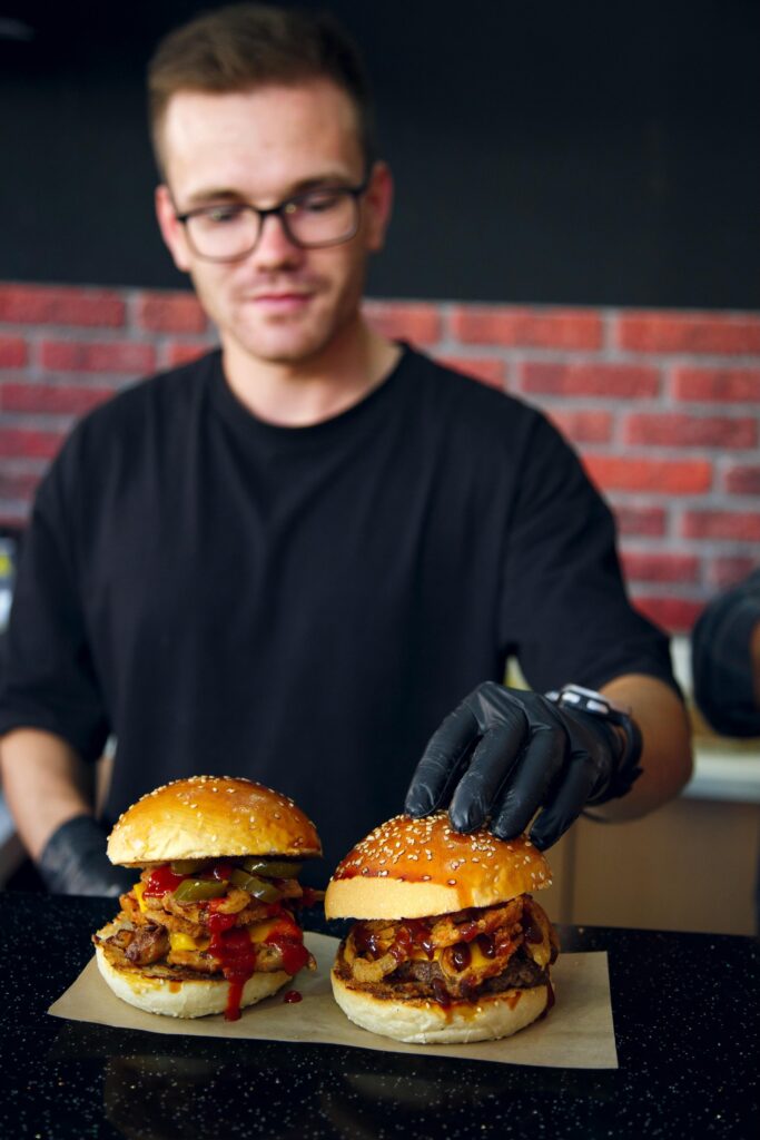 Cuisinier terminant de dresser deux burgers pour une commande dans son Fast Food.