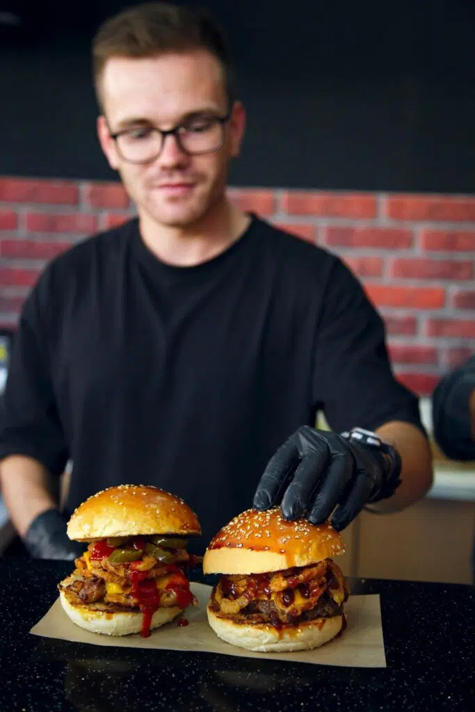 Cuisinier terminant de dresser deux burgers pour une commande dans son Fast Food.
