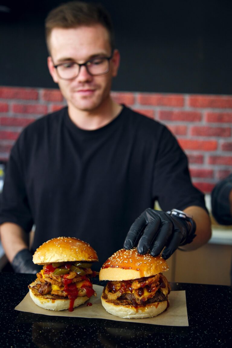 Cuisinier terminant de dresser deux burgers pour une commande dans son Fast Food.