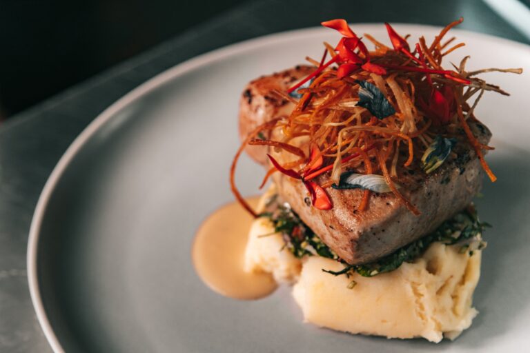 Plat gastromique d'un morceaux de viande, avec sa sauce et ses légumes, délicatement posé sur une purée.
