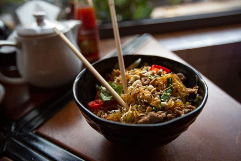 Bol de nouilles asiatiques aux cacahuètes et légumes, baguettes posées dedans.