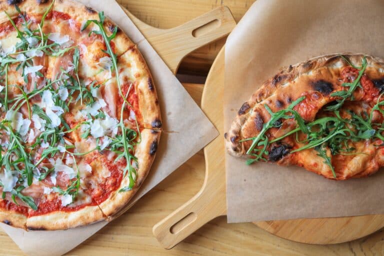 Deux pizzas artisanales garnies de roquette et parmesan sur pelles en bois.