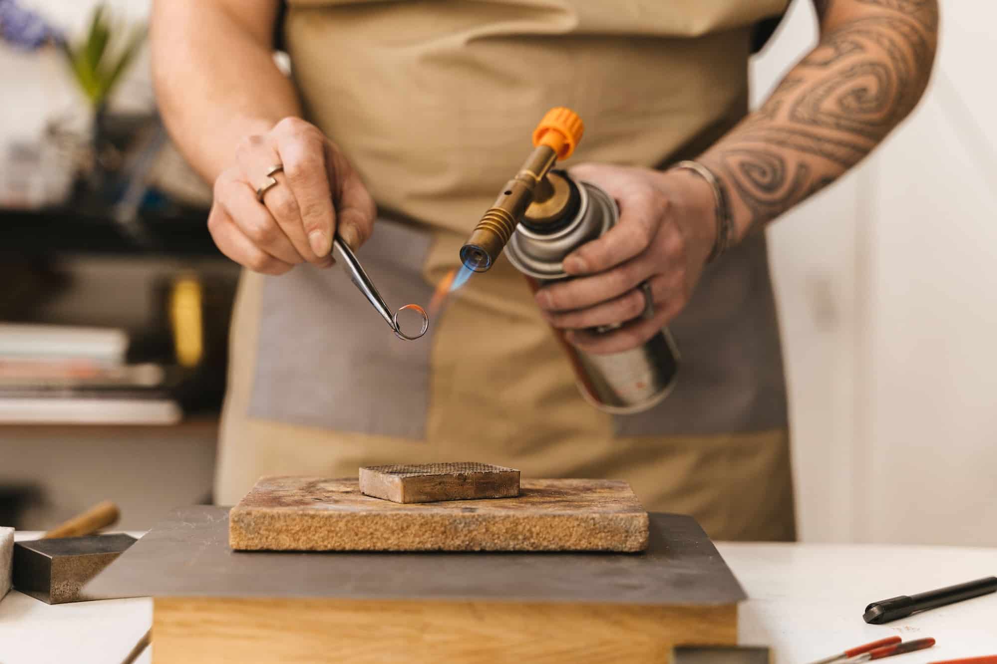 Bijoutier artisanal travaillant une bague au chalumeau dans son atelier.