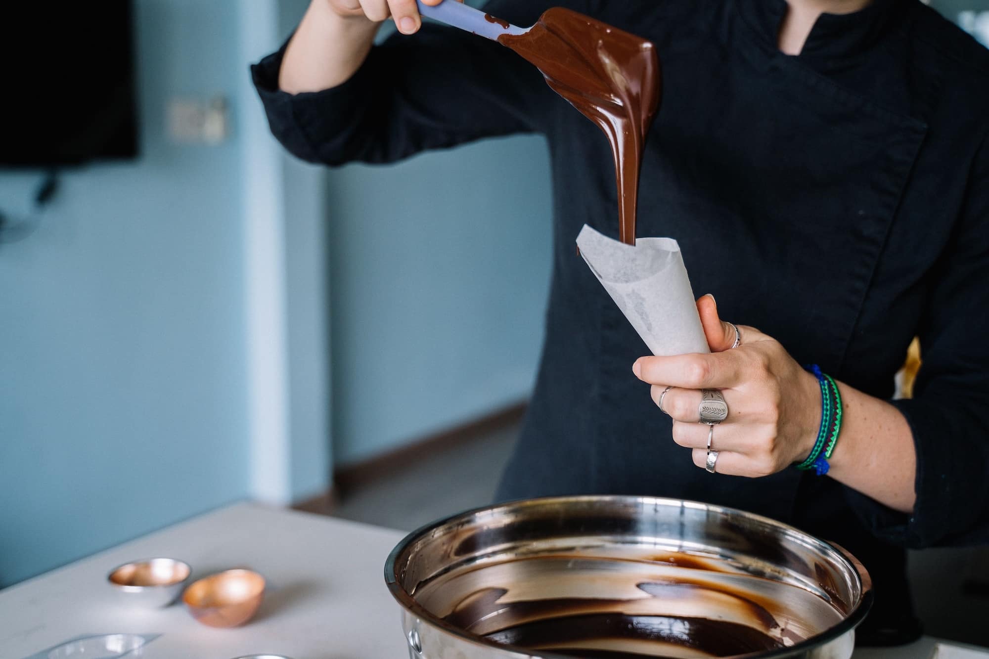 Artisan chocolatier versant du chocolat fondu dans un cornet en papier.