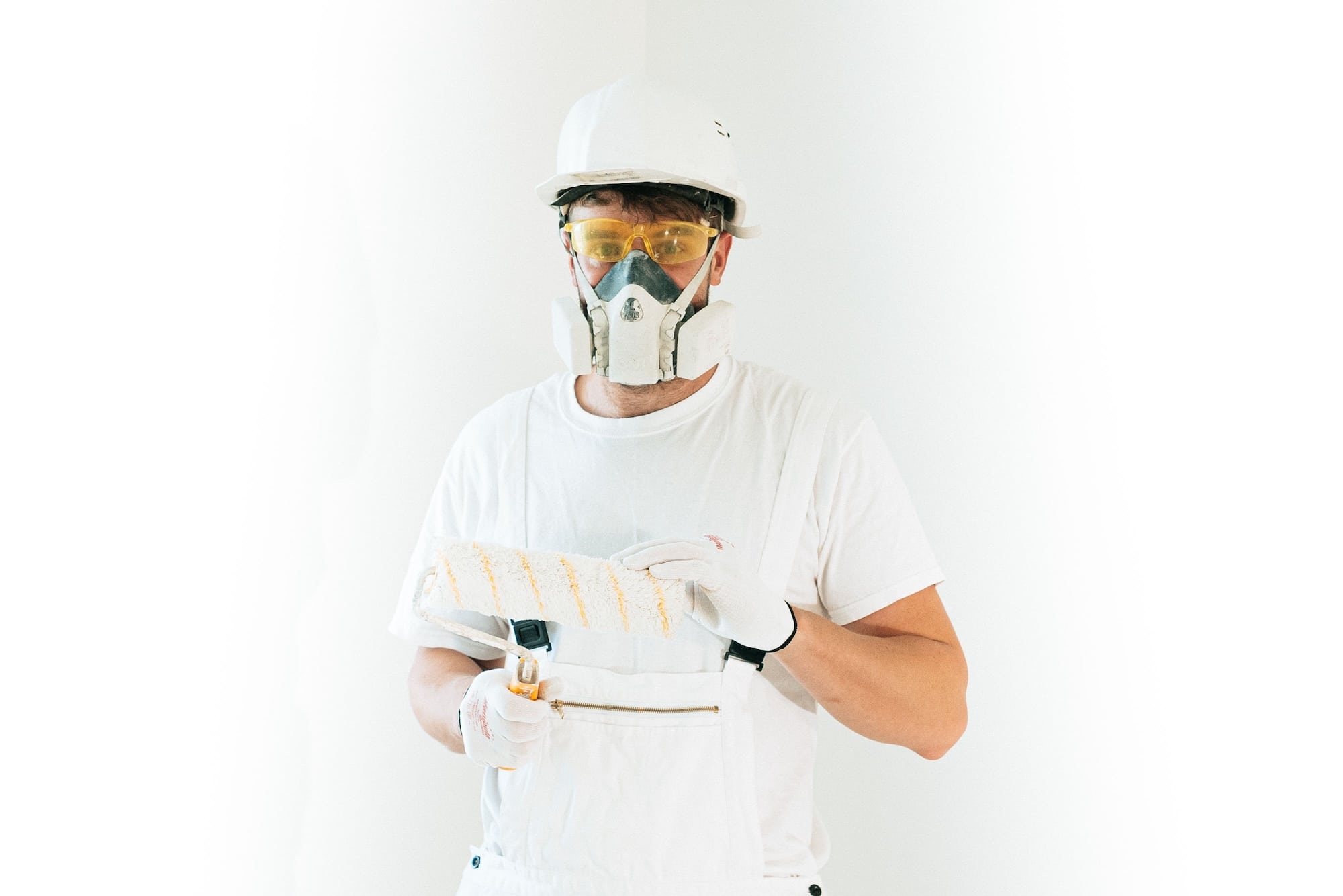 Artisan peintre en bâtiment équipé d'un masque et d'un rouleau de peinture.