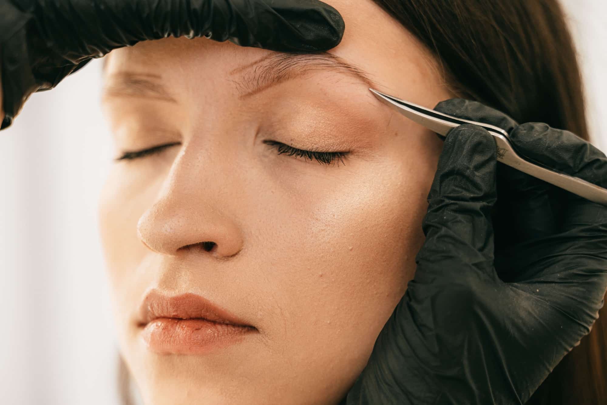 Esthéticienne réalisant une épilation de précision sur les sourcils d'une cliente.